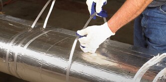 Hand inserting a 3M firestop plug into a wall opening.
