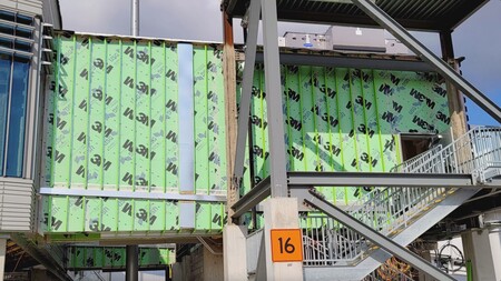 A construction worker wearing gloves to apply a large adhesive sticker to a yellow surface.
