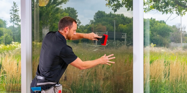 man applies window film to window
