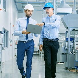 Two factory employees walking and discussing work with a laptop in hand