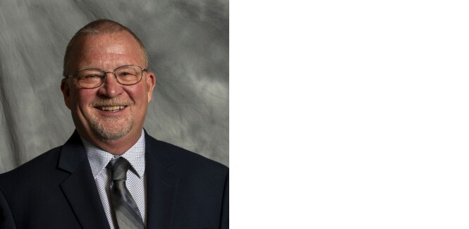 Portrait of Jeffrey O. Emslander against gray textured cloth background.
