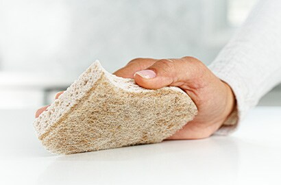 A hand cleaning a table with a Scotch-Brite&reg; Greener Clean Sponge
