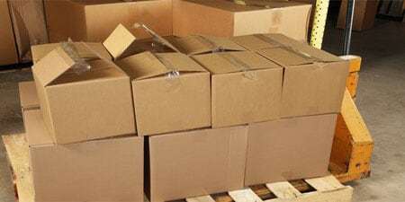 Multiple cardboard boxes stacked on a wooden pallet, showing several with open or poorly sealed top flaps.
