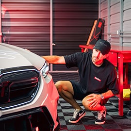 A technician kneels beside a car in a 3M Pro Shop garage, demonstrating service supported by warranty coverage.