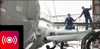 Technicians working on a shiny airplane fuselage in a hangar, featuring a sound wave noise-reduction icon.
