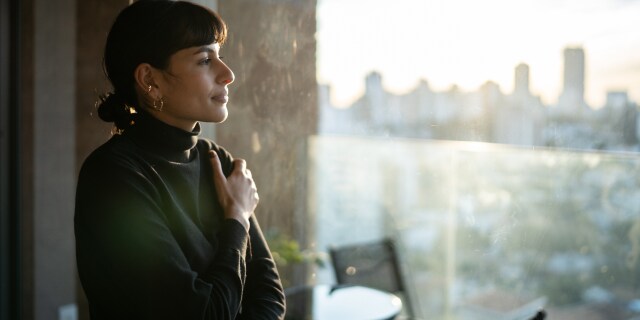 Person standing beside a window overlooking a city skyline.
