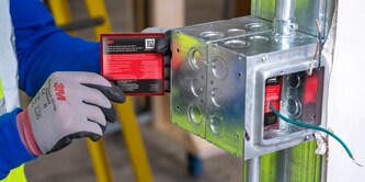 A person wearing gloves applies a 3M fire protection pad to an electrical box.
