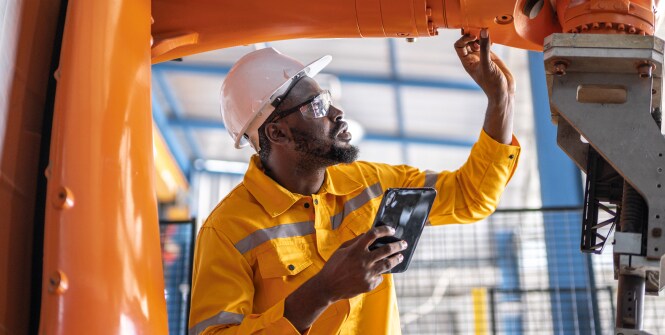 A worker in a yellow safety uniform and a white hard hat inspects machinery in an industrial setting.
