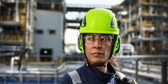 Industrial worker in high‑visibility safety helmet at a manufacturing facility.
