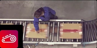 Overhead view of a worker monitoring cardboard boxes moving along a warehouse conveyor belt, featuring a belt icon.
