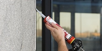 A person applies sealant to the edge of a wall using a caulking gun.
