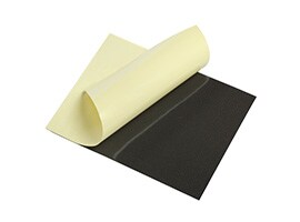 A rolled sheet of light‑colored adhesive material resting on a dark foam gasket surface.