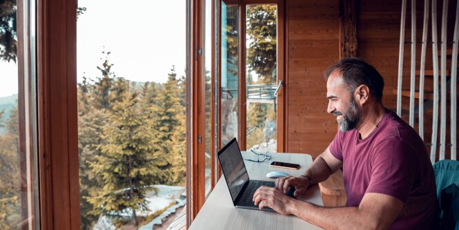man sitting at desk with computer in front of windows 

