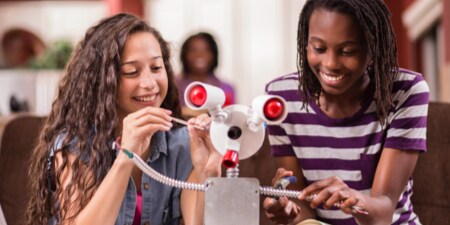 Two smiling, young girls putting together a science experiment.
