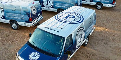 Several vans with blue and white vehicle graphics showcase a business’s logo and vital information.
