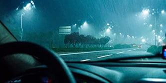 Image of view from in a car looking straight ahead to the road, it's night and it's raining, and there is a reflective tape on the road.
