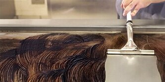 In a commercial kitchen, a woman with a clipboard points up as a chef looks on.
